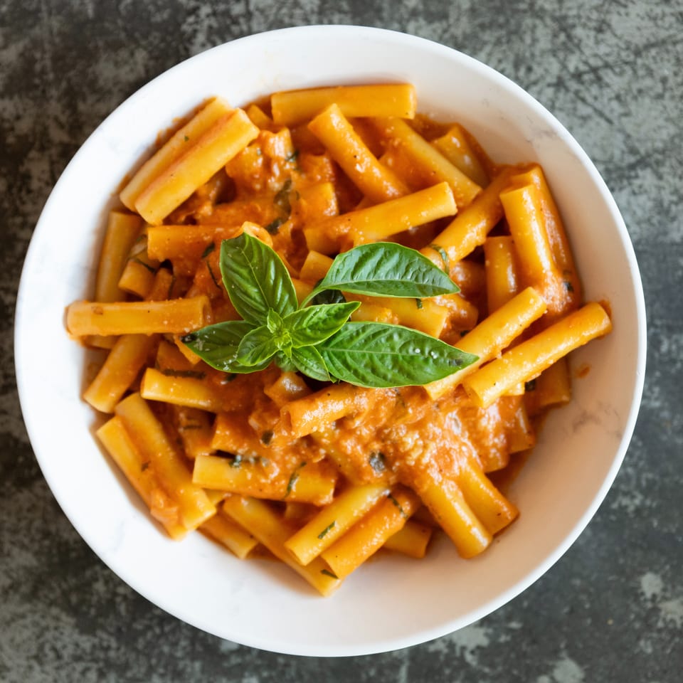 Bowl of rigatoni pasta coated in creamy tomato sauce and garnished with fresh basil leaves.