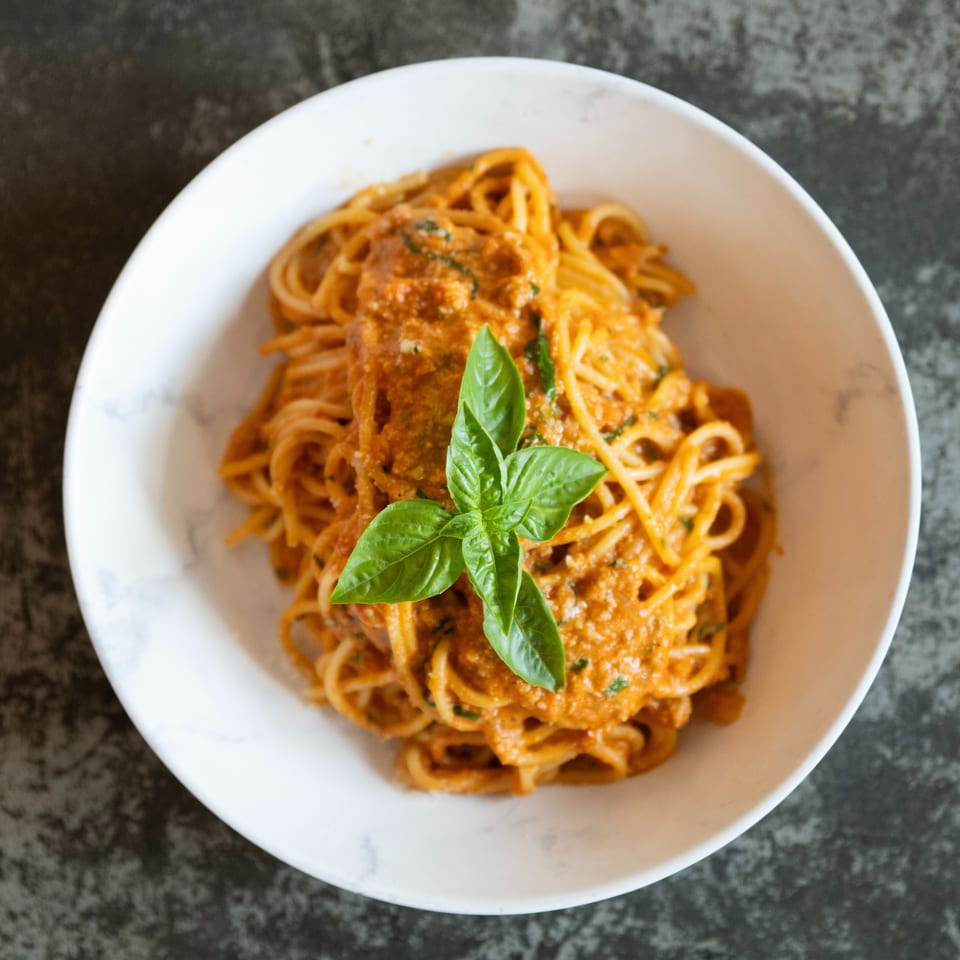 Spaghetti coated in creamy tomato sauce, topped with fresh basil, served in a white bowl on a dark countertop.