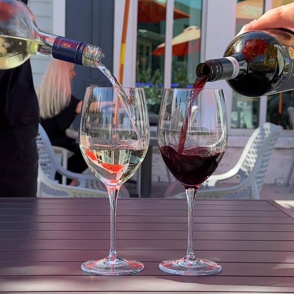 White and red wine being poured into glasses on an outdoor patio table.