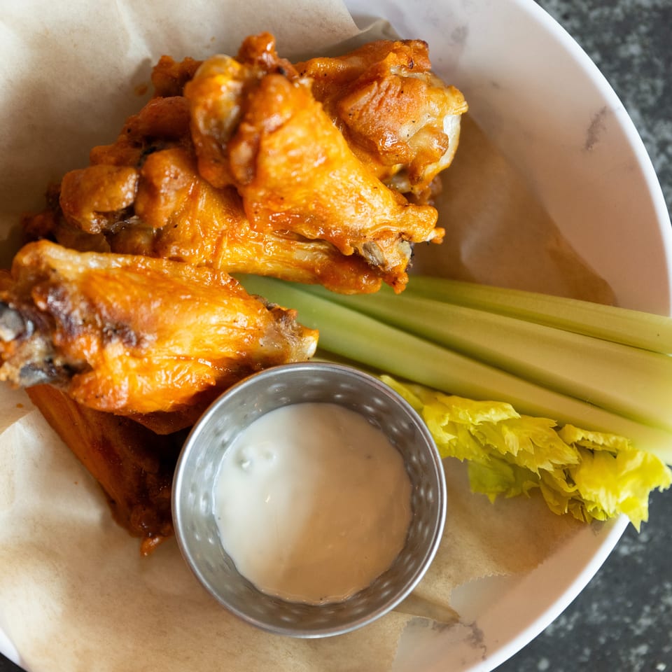 Buffalo chicken wings served with celery sticks and creamy dipping sauce on a paper-lined plate.